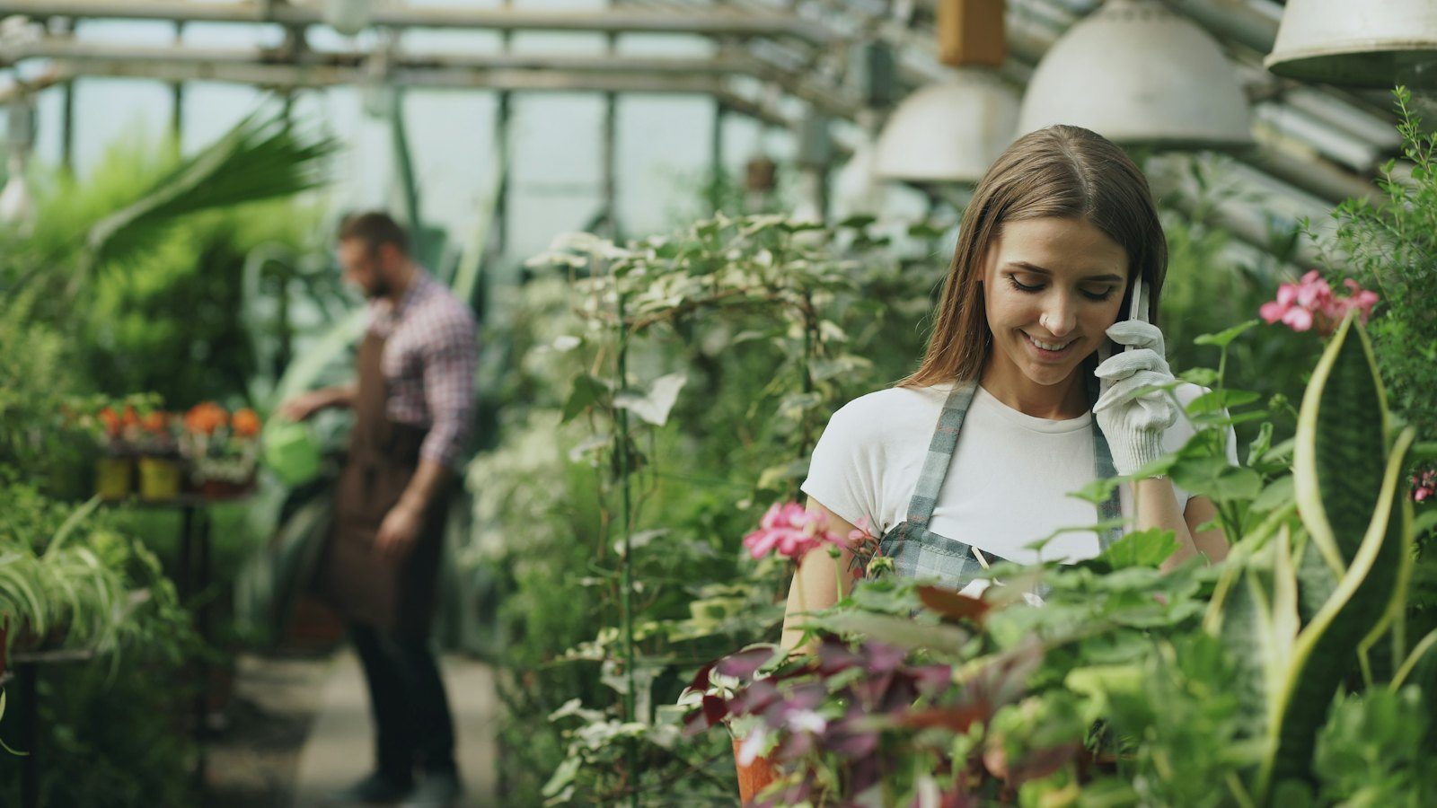 Gardener in an apron talking on her phone among plants in a greenhouse